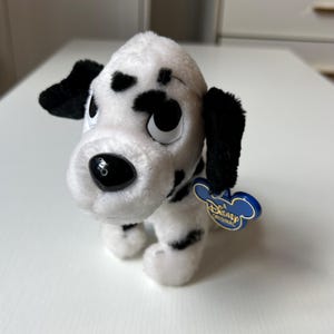 May include: A set of three ceramic mugs with a speckled, cream-colored glaze. Each mug features a different hand-painted design: a blue and green leaf, a yellow flower, and a red berry. The mugs have a simple, modern design.