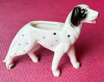Op de afbeelding: Een witte keramische hondenfiguur met zwarte vlekken en markeringen, ontworpen met een plantenbakopening op de rug. De hond heeft zwarte markeringen op zijn oren en rond één oog. Een decoratief item.