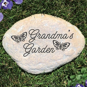 May include: A light gray stone garden marker with the text "Grandma's Garden" and two black butterfly silhouettes.