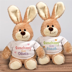 May include: Two brown plush bunny rabbits wearing white t-shirts with the text "Somebunny loves" and a name. The bunny on the left has the name "Olivia" and the bunny on the right has the name "Jacob".