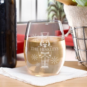 May include: A clear glass wine glass with a personalized design featuring a nutcracker and snowflakes. The text "THE HINKLEYS" is etched on the glass.