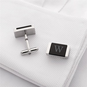 May include: A pair of silver cufflinks with black rectangular inserts. One cufflink has a black onyx insert with the letter "W" engraved on it.