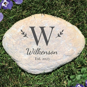 May include: A light gray stone with the letter "W" and the text "Wilkenson Est. 2023" engraved on it. The stone is surrounded by green grass.