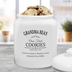 May include: White ceramic cookie jar with black text that reads "Grandma Bea's Oven Fresh Cookies made special for Carson Cassie Thomas Lizzy Emmett Fin Reilly".
