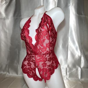 May include: A red lace bodysuit with a halter neck design. The lingerie features a floral pattern and a scalloped trim. The open crotch design adds a unique detail to this intimate apparel.