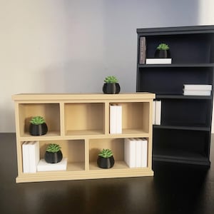 Puede incluir: Se muestran dos estanter&iacute;as en miniatura, una beige y otra negra. La estanter&iacute;a beige tiene seis compartimentos con peque&ntilde;os libros blancos y plantas en macetas negras. La estanter&iacute;a negra tiene tres compartimentos con art&iacute;culos similares. Los art&iacute;culos est&aacute;n dispuestos sobre una superficie negra.