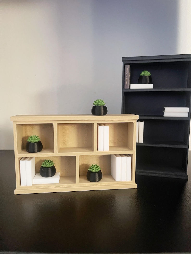 Puede incluir: Se muestran dos estanter&iacute;as en miniatura, una beige y otra negra. La estanter&iacute;a beige tiene seis compartimentos con peque&ntilde;os libros blancos y plantas en macetas negras. La estanter&iacute;a negra tiene tres compartimentos con art&iacute;culos similares. Los art&iacute;culos est&aacute;n dispuestos sobre una superficie negra.