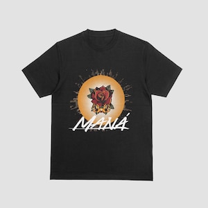 Może przedstawiać: Czarny t-shirt z grafiką czerwonej róży z żółtymi akcentami, na tle żółtego wzoru promieni słonecznych. Słowo "MANÁ" jest napisane białym pismem poniżej. Koszulka ma okrągły dekolt.