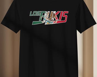 May include: Black t-shirt featuring the text "LOS BUKIS" in white, green, and red. The word "BUKIS" is filled with a design that resembles the Mexican flag. The shirt is a classic crew neck style.