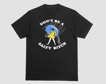 May include: Black t-shirt with the text "DON'T BE A SALTY BITCH" in white. The graphic shows a person in a yellow dress holding a blue umbrella in the rain. The person is walking and salt is pouring from the umbrella.
