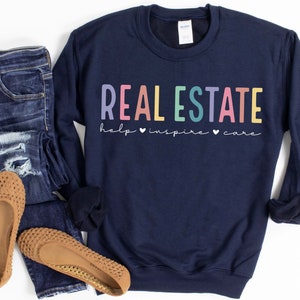 May include: Navy blue sweatshirt with the text "REAL ESTATE help &hearts; inspire &hearts; care" in rainbow colors.
