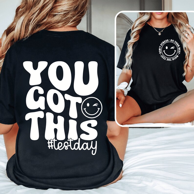 Pu&ograve; includere: T-shirt nero con testo bianco e una faccina sorridente che fa l'occhiolino. La parte posteriore della maglietta dice "YOU GOT THIS #testday" in un font retr&ograve;. La parte anteriore della maglietta ha un piccolo disegno circolare con una faccina sorridente e le parole "Don't Stress - Do Your Best - Rock The Test".