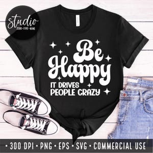 May include: Black t-shirt with white text that reads "Be Happy It Drives People Crazy". The text is in a retro font style with stars around it.