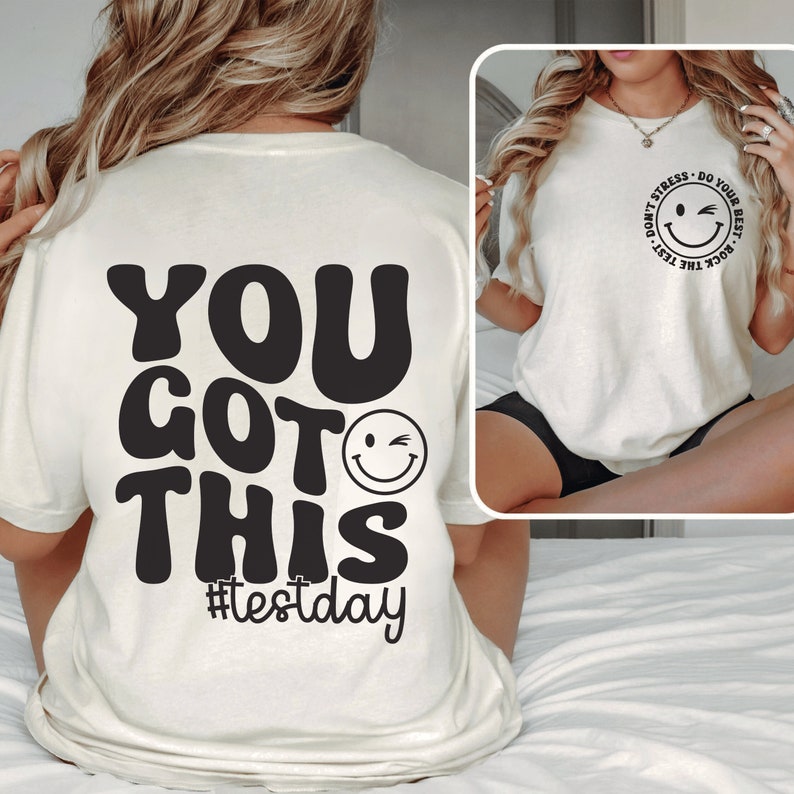 Pu&ograve; includere: T-shirt color crema con la scritta "YOU GOT THIS" in grandi caratteri neri in stile retr&ograve;. Sotto il testo c'&egrave; una faccina sorridente che fa l'occhiolino, con l'hashtag "#testday" sotto. La maglietta presenta anche un disegno pi&ugrave; piccolo con una faccina sorridente che fa l'occhiolino e la scritta "DON'T STRESS - DO YOUR BEST - ROCK THE TEST".