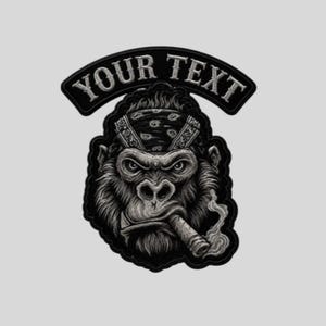 Puede incluir: Un parche bordado en blanco y negro que muestra un gorila con un pañuelo estampado y fumando un cigarro. Sobre el gorila, una pancarta curva contiene el texto YOUR TEXT en una fuente serif negrita. El diseño presenta un estilo detallado y sombreado.