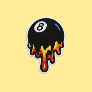May include: An embroidered patch featuring a black billiard ball with the number eight in white. The bottom of the ball appears to be melting, with drips in shades of yellow, orange, and red. The entire design is outlined in white thread.