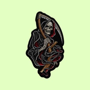 Könnte beinhalten: Ein Stoffaufnäher mit einer Illustration des Sensenmanns mit Totenkopfgesicht, der eine schwarze Kapuzenrobe mit rotem Innenfutter trägt und eine große Sense mit Holzstiel und Metallklinge hält, umrandet mit einem dicken schwarzen Rand.