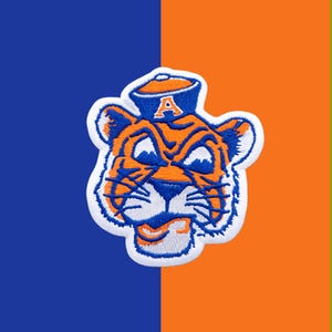Könnte beinhalten: Ein gestickter Aufnäher mit einem Tigerkopf, der eine blaue Matrosenmütze mit dem Buchstaben A in Orange trägt. Der Tiger ist orange mit blauen Streifen und weißen Akzenten, umrandet mit weißem Garn auf einem blau-orangen Hintergrund.