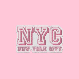 May include: A white embroidered patch featuring the letters NYC in a large, bold, pink-outlined collegiate font, with the words NEW YORK CITY written in a smaller, matching pink-outlined font directly underneath the main letters.