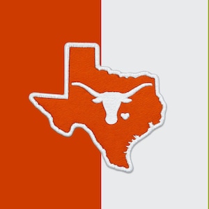 Könnte beinhalten: Ein gestickter Aufnäher in Form des Bundesstaates Texas mit einem gebrannten orangefarbenen Hintergrund und einem weißen Rand. Das Design zeigt eine weiße Silhouette eines Longhorn-Rinderkopfes in der Mitte, begleitet von einem kleinen weißen Herz.