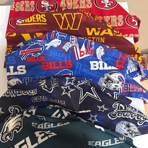 May include: A stack of five fabric scrub caps featuring various NFL team logos and colors. The top cap is red with 49ers branding, followed by a burgundy Washington cap, a blue Buffalo Bills cap, a black Dallas Cowboys cap, and a dark green Eagles cap.