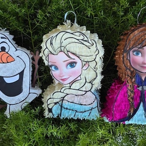 Puede incluir: Tres pi&ntilde;atas con forma de personajes: Olaf el mu&ntilde;eco de nieve, Elsa y Anna. Olaf tiene una nariz de zanahoria y una gran sonrisa. Elsa tiene el pelo rubio y un vestido azul. Anna tiene trenzas marrones y una capa rosa.
