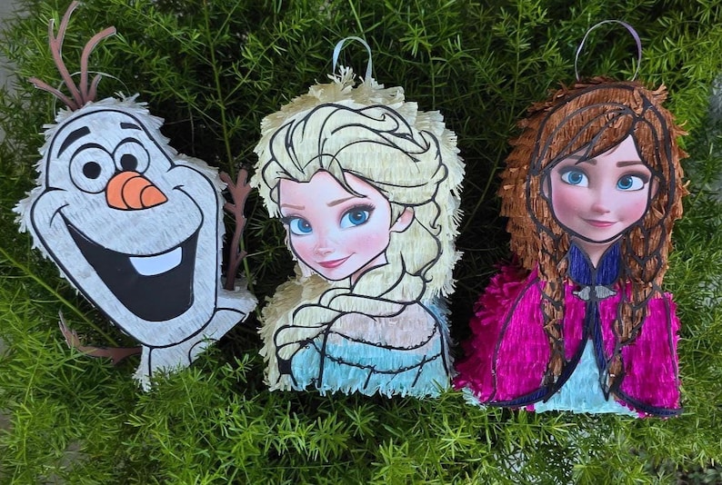 Pu&ograve; includere: Tre colorate pi&ntilde;atas con personaggi del film d'animazione. Olaf il pupazzo di neve, Elsa e Anna sono raffigurati con tratti del viso dettagliati e colori vivaci. Ogni pi&ntilde;ata ha un anello per appenderla, su uno sfondo di fogliame verde.