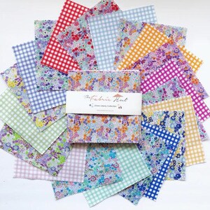 May include: A stack of square fabric swatches arranged in a fan pattern, featuring various floral prints and gingham checks in red, blue, yellow, green, and purple. A white paper band wraps the center with the text The Fabric Hut.