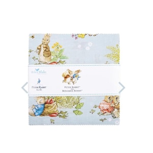 May include: A stack of fabric squares featuring a light blue background with illustrations of Peter Rabbit and Benjamin Bunny, green foliage, and carrots. A white paper band wraps around the center with the text Riley Blake Designs Peter Rabbit and Benjamin Bunny.