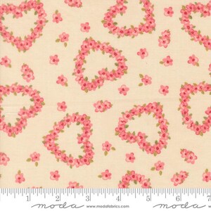 May include: A cream-colored fabric featuring a repeating pattern of pink floral hearts and scattered individual pink flowers with small green leaves. A white ruler is visible at the bottom edge, showing measurements in inches up to 7 inches.