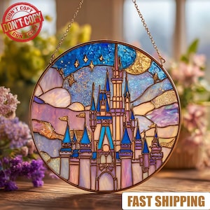 May include: Round stained glass window art featuring a fairytale castle with blue, pink, and gold accents. The castle is set against a night sky with stars and a crescent moon. The artwork is framed in a gold metal border.