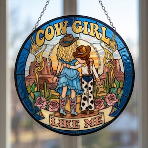 May include: A circular stained glass suncatcher featuring two figures in cowboy hats standing in a desert landscape with cacti and roses. The text reads COW GIRL at the top and LIKE ME at the bottom, with I KNEW YOU written on both sides.