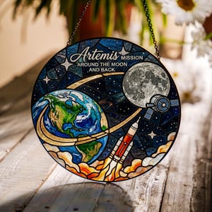 Pu&ograve; includere: Opera d'arte circolare in vetro colorato raffigurante la missione Artemis. Il design presenta la Terra, la luna, un lancio di razzo e un satellite su uno sfondo stellato. Il testo recita "Artemis Mission Around the Moon and Back."