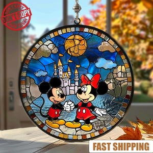 Op de afbeelding: Rond gebrandschilderd glazen raam met Mickey en Minnie Mouse voor een kasteel, onder een gele maan en blauwe lucht. Het kunstwerk heeft een zwarte rand en wordt opgehangen door een zilveren ketting. De woorden "DON'T COPY" staan linksboven.