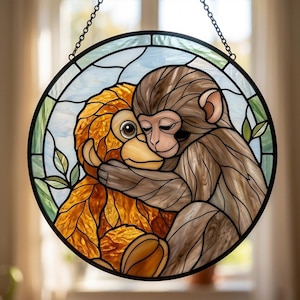 May include: Round stained glass window art featuring two embracing monkeys. One monkey is brown, the other is orange. The background is blue and green with leaf accents. The window is framed in black and hangs from a chain.