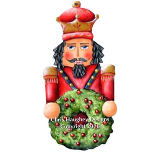 May include: A hand-painted wooden nutcracker ornament holding a green wreath with red berries. The nutcracker is wearing a red and gold uniform with a crown. The ornament is signed "Chris Haughey Designs Copyright 2016".