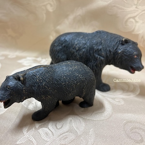May include: Two black bear figurines. One bear is standing, the other is in a walking position. The bears have textured fur and red accents in their mouths and eyes. The figurines are likely made of a hard material.