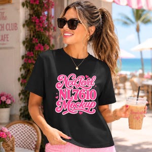 May include: A black t-shirt with the text "Next Level NL7610 Mockup" in pink script. The woman in the image is wearing sunglasses and holding a beverage. The background includes flowers and a cafe.