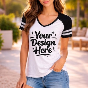 Può includere: T-shirt bianco con scollo a V con maniche nere e scollatura nera. Le maniche hanno due strisce grigie. Il testo "Your Design Here" è stampato in nero sul davanti della maglietta. La maglietta è abbinata a pantaloncini di jeans blu.