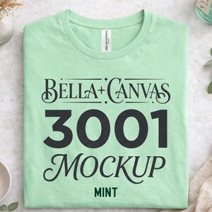 May include: A mint green Bella+Canvas 3001 mockup t-shirt. The shirt displays the Bella+Canvas logo and the text "3001 MOCKUP" in black, with "MINT" in green at the bottom. The t-shirt is neatly folded.