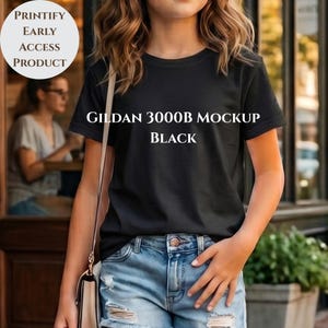 Könnte beinhalten: Ein schwarzes Gildan 3000B Mockup T-Shirt. Das T-Shirt wird von einer Person mit hellblauen Jeansshorts getragen. Der Text "GILDAN 3000B MOCKUP BLACK" ist auf das T-Shirt gedruckt. Ein weißer Kreis mit dem Text "PRINTIFY EARLY ACCESS PRODUCT" befindet sich in der oberen linken Ecke.