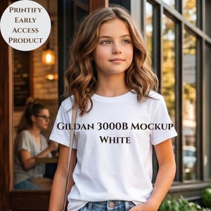 Könnte beinhalten: Ein weißes Gildan 3000B Mockup-T-Shirt wird von einer Person getragen. Das Shirt hat einen klassischen Rundhalsausschnitt und kurze Ärmel. Der Text "GILDAN 3000B MOCKUP WHITE" ist auf der Vorderseite aufgedruckt. Eine kreisförmige Grafik mit dem Text "PRINTIFY EARLY ACCESS PRODUCT" befindet sich oben links.