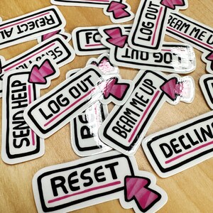 Könnte beinhalten: Eine Sammlung weißer Aufkleber mit schwarzen Umrissen und rosafarbenem Text. Die Aufkleber haben verschiedene Sätze, darunter "Send Help", "Log Out", "Beam Me Up", "Reset" und "Reject All".