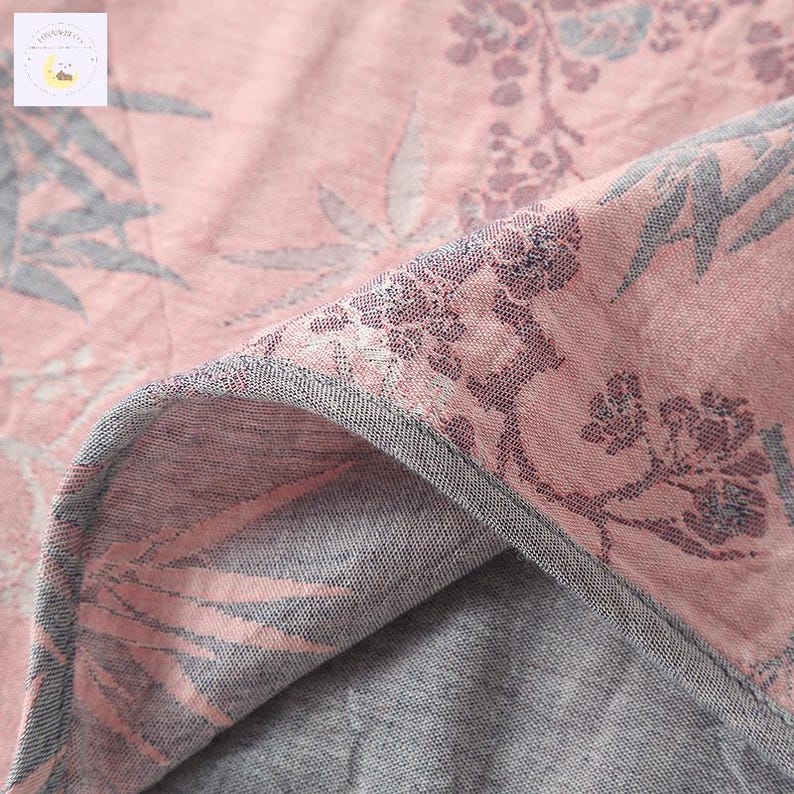 May include: Close-up of a pink floral fabric with gray accents. The fabric features a detailed pattern of flowers and leaves, with a gray border. The design is visible on both sides of the folded fabric, creating a layered effect.
