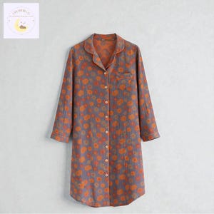 May include: A long-sleeved, button-down nightgown in a floral pattern. The gown is primarily gray with orange and yellow flowers. It has a collar, a chest pocket, and white trim along the edges.