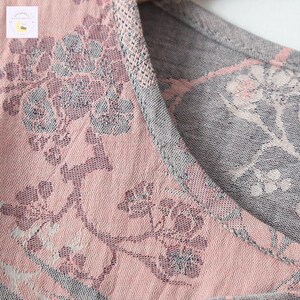 May include: Close-up of a pink and gray floral patterned fabric. The fabric has a delicate, woven texture with a repeating design of flowers and leaves. The neckline is trimmed with a gray knit fabric.