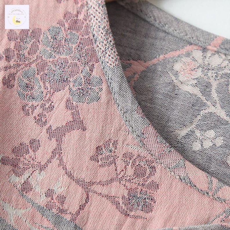 May include: Close-up of a pink and gray floral patterned fabric. The fabric has a delicate, woven texture with a repeating design of flowers and leaves. The neckline is trimmed with a gray knit fabric.