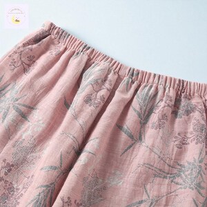 May include: Close-up of pink fabric with an elastic waistband. The fabric features a floral pattern in shades of gray. The material appears soft and lightweight, suggesting it could be used for sleepwear or casual wear.