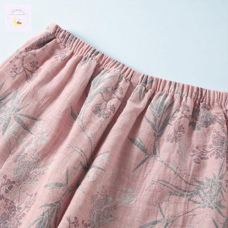 May include: Close-up of pink fabric with an elastic waistband. The fabric features a floral pattern in shades of gray. The material appears soft and lightweight, suggesting it could be used for sleepwear or casual wear.