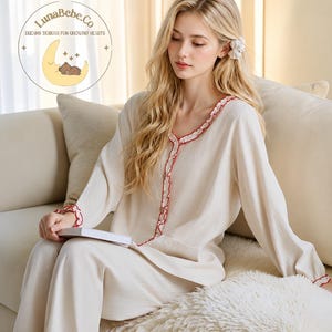 May include: Cream-colored pajama set with red ruffle trim. The long-sleeved top and pants are made of a soft fabric. The image includes the LunaBebe.Co logo with the text "Dreamy Designs for Growing Hearts".